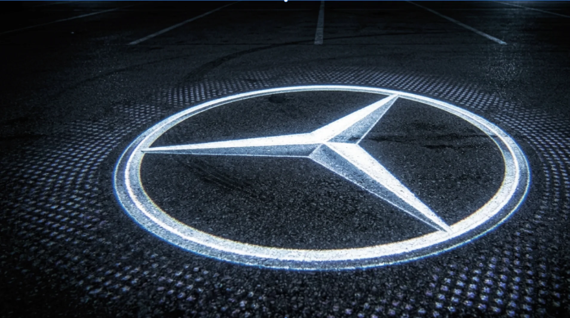 Emblema automobilistico a tre punte illuminato sull’asfalto scuro